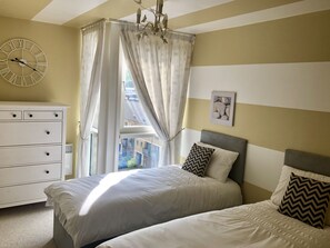 A bedroom with a bed, a dresser, a clock, and a window with curtains. - Toothbrush Apartments - Ipswich Waterfront - Anchor St (Ipswich)