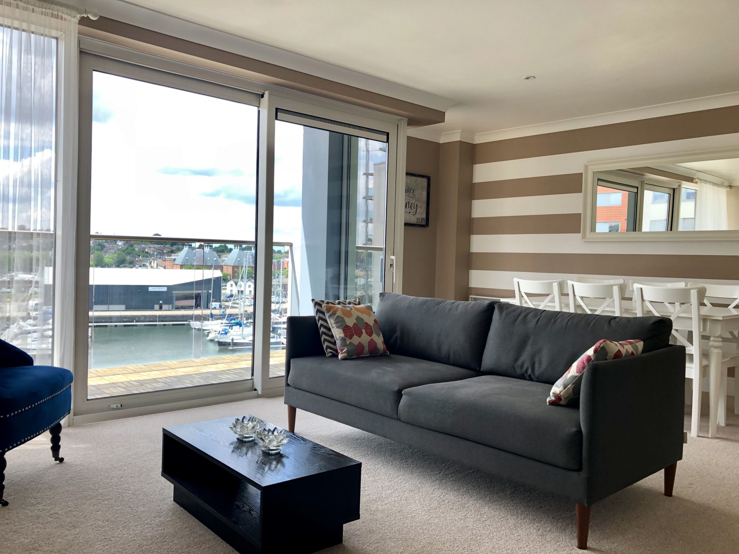 A modern living room with a grey sofa, a black coffee table, and a view of a marina through large windows.
