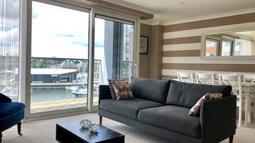 A modern living room with a grey sofa, a black coffee table, and a view of a marina through large windows.