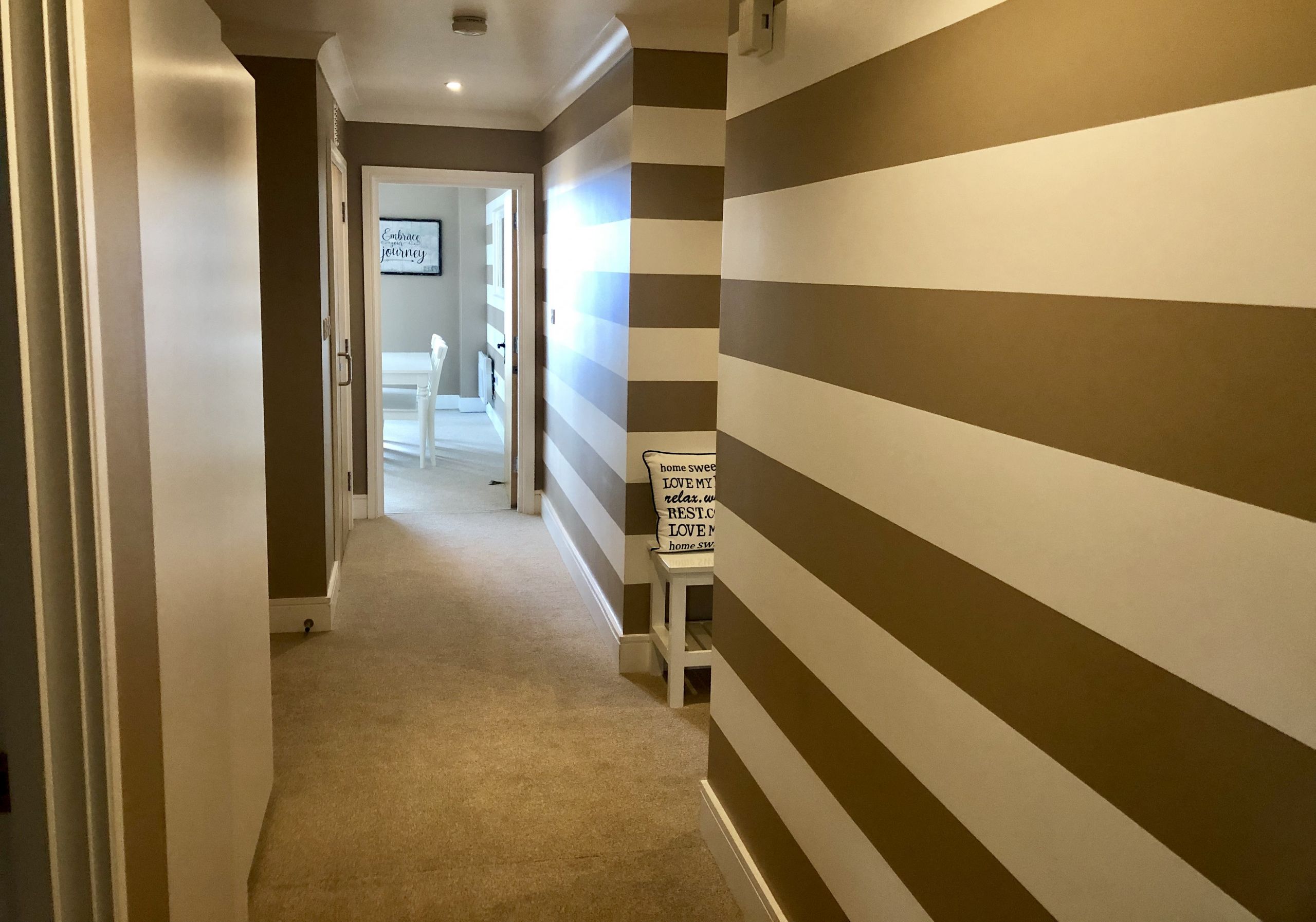A hallway with striped walls, a carpeted floor, and a sign on a small table.