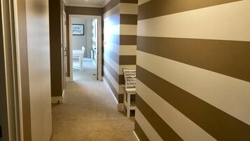 A hallway with striped walls, a carpeted floor, and a sign on a small table.