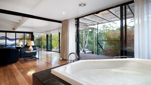A modern bathroom with a large bathtub, wooden flooring, and a view of the outdoors. - Centrally located 2-bedroom luxury villa in Australia’s spa country (Hepburn Springs)