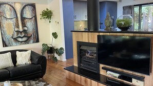 A modern living room with a large flat-screen TV, a fireplace, and a black leather sofa. - Centrally located 2-bedroom luxury villa in Australia’s spa country (Hepburn Springs)