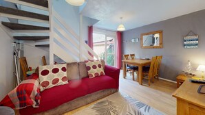 A cozy living room with a red sofa, wooden dining table, and a staircase. - 24 Strawberry Hill, Tolroy Manor (Hayle)