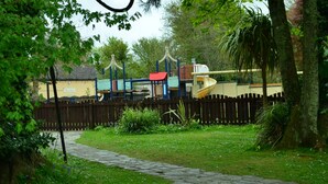 A playground with a wooden fence, a yellow building, and a stone pathway. - 24 Strawberry Hill, Tolroy Manor (Hayle)