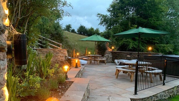 Eine Außenpatio-Terrasse mit Steinböden, Holztischen und grünen Sonnenschirmen.