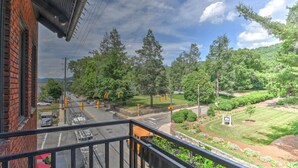Vista de uma varanda com vista para uma rua com semáforos, uma área arborizada e uma cordilheira ao longe.