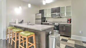 Uma cozinha moderna com ilha central, eletrodomésticos de aço inoxidável e banquetas de madeira.