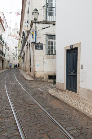 A narrow street with cobblestone pavement and a tram track. Buildings line the street, and there are signs and a flag visible.