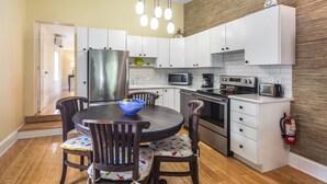 A modern kitchen with white cabinets, a stainless steel refrigerator, a microwave, a stove, and a toaster. There is a dining table with chairs and a bowl of fruit. - ~HORSE CONCH~ Amazing location with shared pool and covered balcony! (Key West)