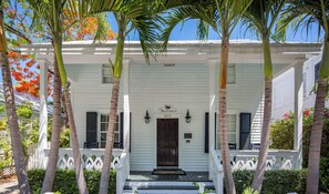 A white building with a dark brown door, a sign reading "Sea Conch 623", and a white picket fence.