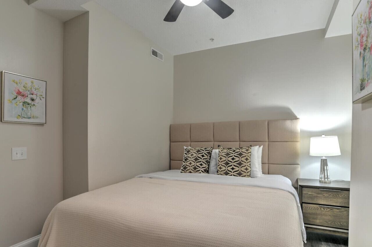 A bedroom with a bed, a headboard, a nightstand, a lamp, and a ceiling fan.