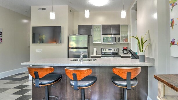 Una cocina moderna con una isla central, taburetes de bar, electrodomésticos de acero inoxidable e iluminación colgante.