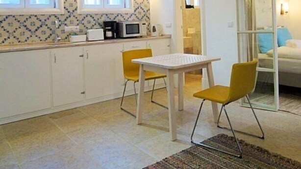 A compact kitchen with white cabinets, a dining table with two chairs, and a large window. - 0 Ophiussa (Lisbon)