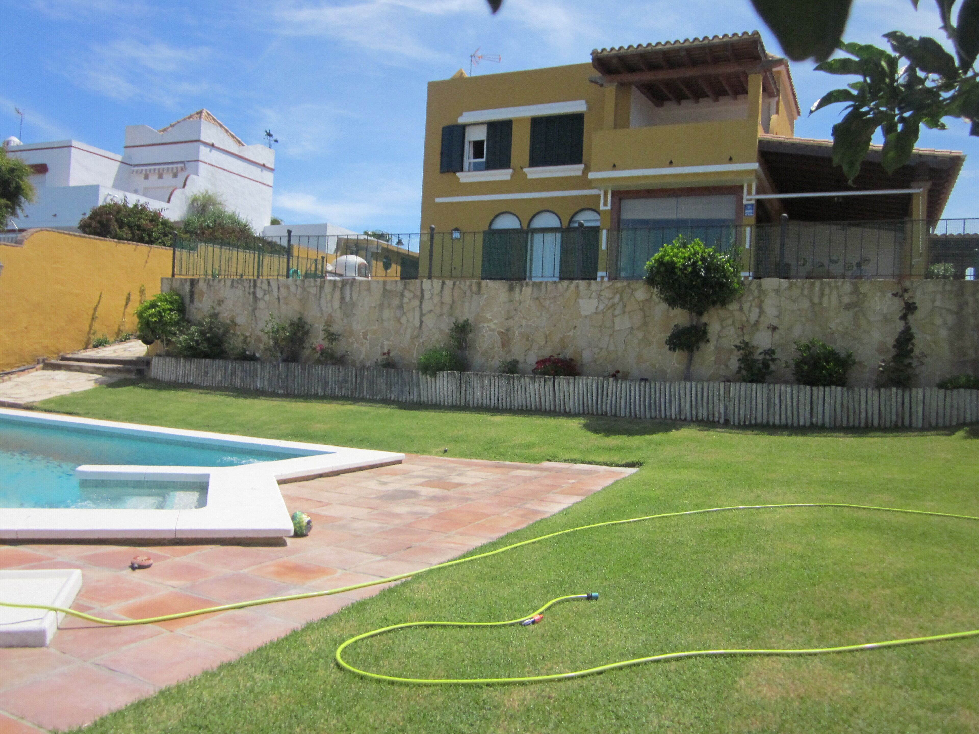 Un barrio residencial con piscina, un muro de piedra y césped bien cuidado.