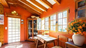 Una cocina con una mesa de madera, sillas, un jarrón grande de flores y una ventana con luz solar.