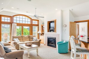 A spacious living room with a fireplace, large windows, and a dining area. - Love R Shack At The Beach: 10-bed Oceanside Duplex (Corolla)