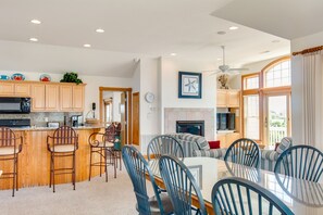 A spacious kitchen with wooden cabinets, a dining area with striped chairs, and a large window providing natural light. - Love R Shack At The Beach: 10-bed Oceanside Duplex (Corolla)