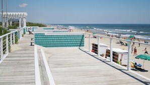 Een wandelpad aan het strand met een houten terras, een uitkijktoren en strandparasols.