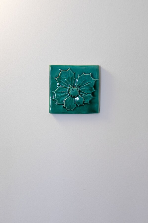 A teal ceramic tile with a cracked design on a plain white wall.