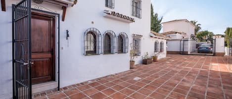 A white building with a tiled patio, a wooden door, and a gate.