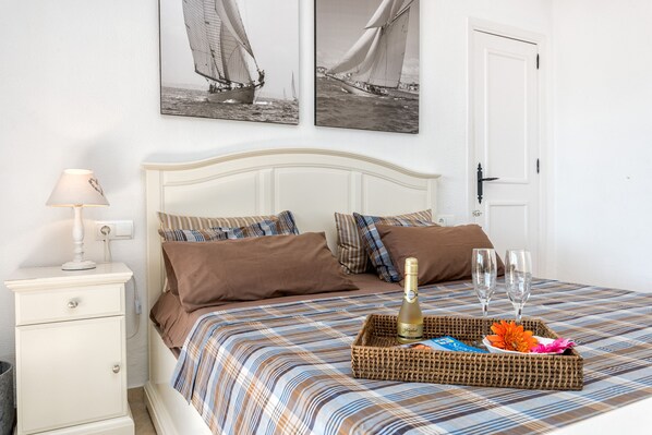 A neatly made bed with a striped bedspread, a bedside table with a lamp, and a tray with a bottle and glasses on the bed.