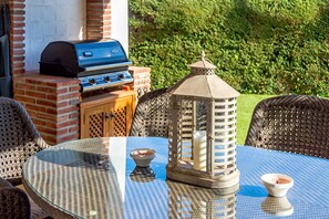 Ein runder Glastisch mit Korbstühlen, einem Grill und einer Laterne.