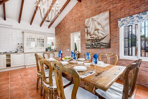 A dining area with a brick wall, wooden chairs, and a large painting.