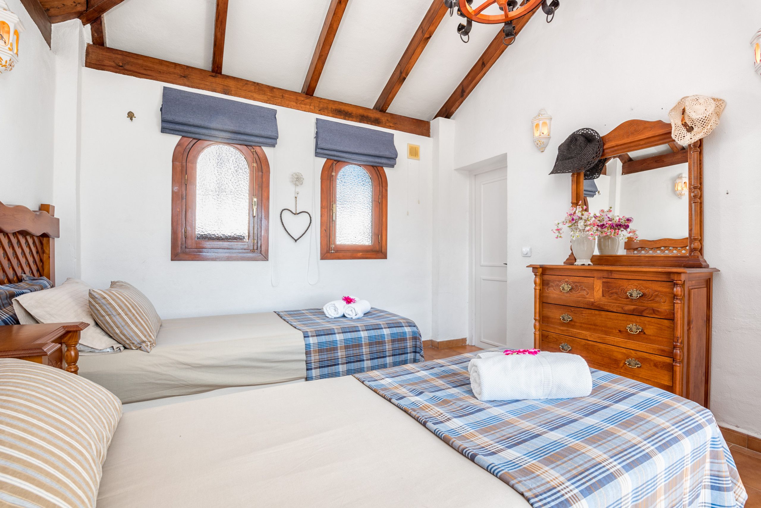 A bedroom with two beds, wooden beams, a dresser, and a mirror.
