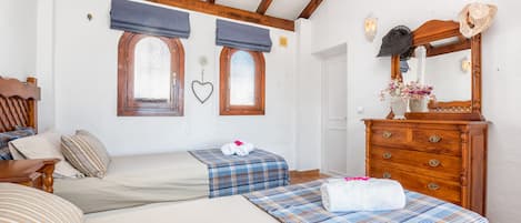 A bedroom with two beds, wooden beams, a dresser, and a mirror.