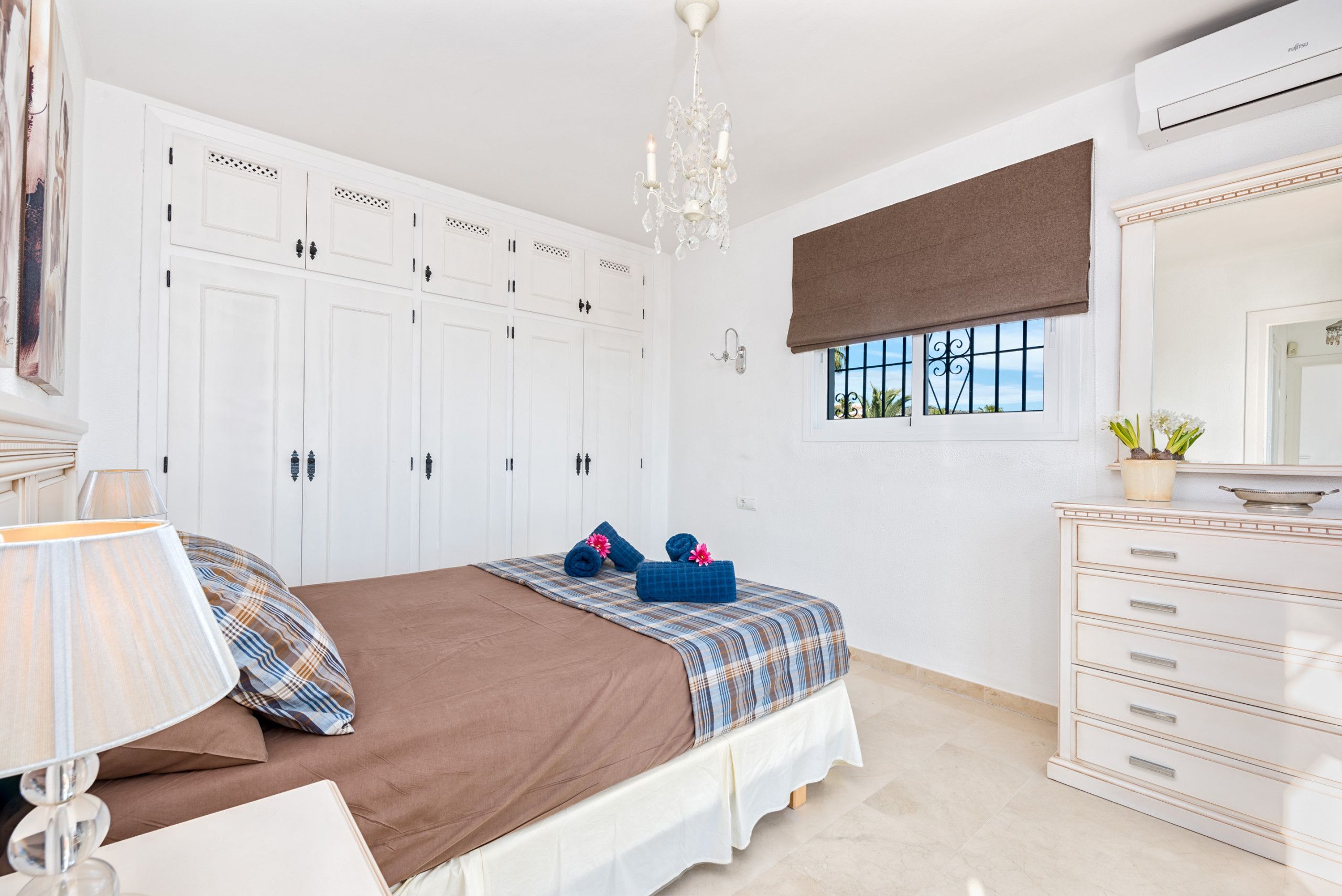 A bedroom with a bed, a dresser, a window with a view, and a chandelier.