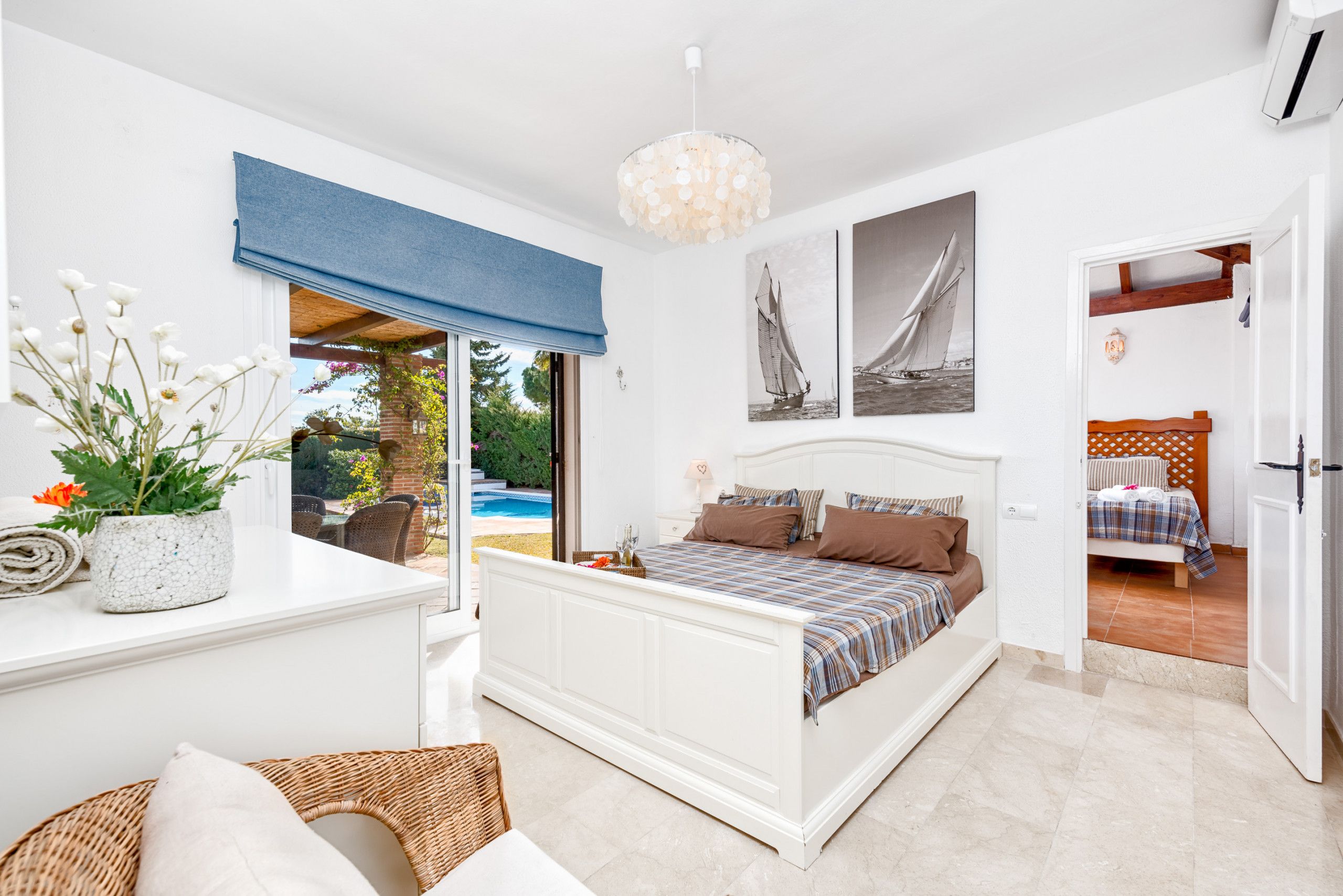 A bedroom with a bed, a bedside table, a potted plant, and a view of the outside.