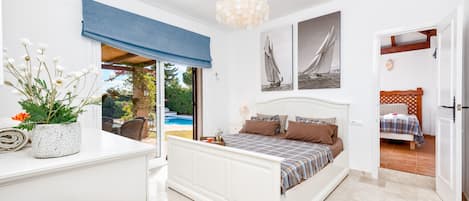 A bedroom with a bed, a bedside table, a potted plant, and a view of the outside.