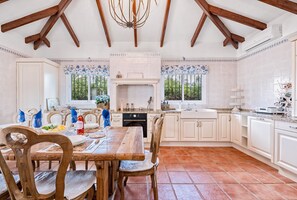 A spacious kitchen with white cabinetry, a dining area with wooden chairs, and a tiled floor.