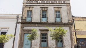 Edifici de dues plantes amb façana enrajolada, una porta blava i un balcó amb barana metàl·lica.