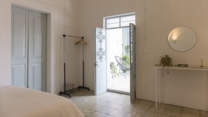 Una habitació amb un llit, una porta, una làmpada de peu, una taula amb una planta i una finestra.