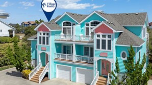A two-story house with a balcony, a garage, and a sign indicating 'Village Realty'. - Love R Shack: Oceanside Duplex, Spa, Shared Pool (Corolla)