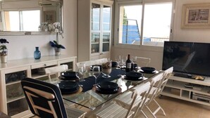 A dining area with a glass table, white chairs, a TV, and a view of the sea. - Spectacular apartment with fantastic panoramic views (Llançà)