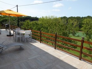 An outdoor patio with a wooden railing, a table, chairs, and a yellow umbrella.