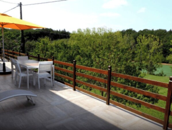 Um deck de madeira com móveis ao ar livre e vista para uma paisagem verde.