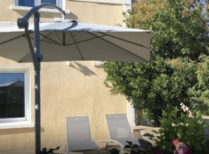 A patio with a white umbrella, two lounge chairs, and a building with beige walls.