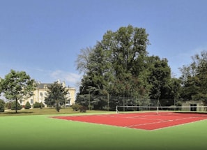 A tennis court with a net, surrounded by trees and a building in the background.