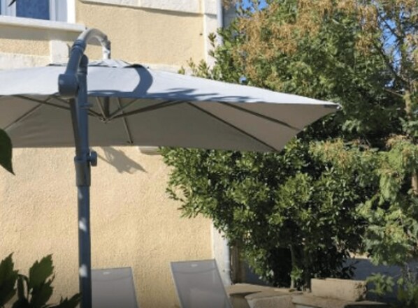 An outdoor umbrella, a beige wall, and green foliage.