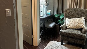 Una habitación acogedora con un sillón estampado, un escritorio pequeño con una lámpara y una planta.