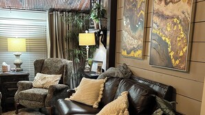 Una sala de estar con un sofá de cuero oscuro, sillones estampados, un cuadro abstracto grande y una planta en maceta.