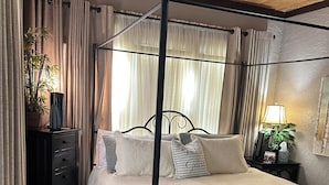 Un dormitorio con cama con dosel, un escritorio con silla, una mesita de noche con lámpara y una planta en maceta.
