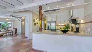 A modern kitchen with white cabinets, a large island with a fruit bowl, and a hanging light fixture.