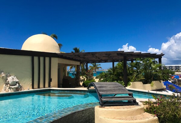 Une piscine avec des chaises longues, une pergola et une vue sur l’océan.