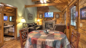 A cozy cabin interior with a wooden ceiling, a fireplace, a television, and a dining area with a quilted tablecloth. - Southern Charm #88 -Charming & Clean Log Cabin! (Sevierville)