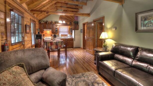 A cozy cabin interior with wooden beams, a dining area, a leather couch, and a kitchen. - Southern Charm #88 -Charming & Clean Log Cabin! (Sevierville)